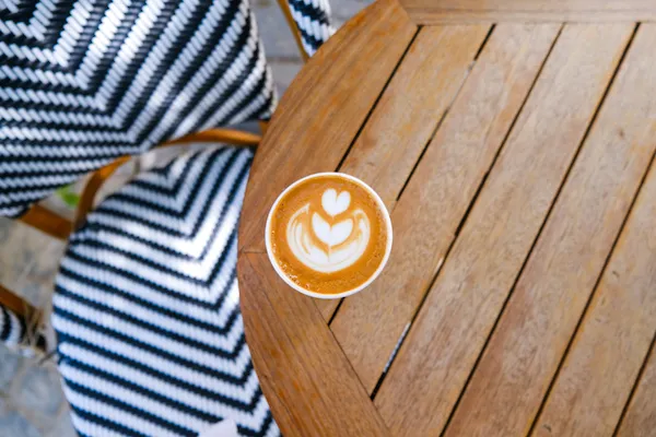 top down perspective of a coffee with foam art in a cup on a cirular wooden table