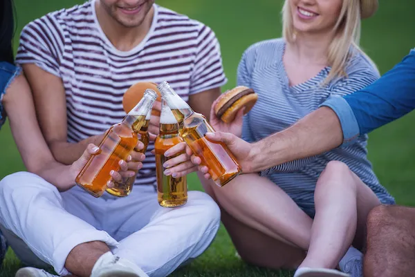 Friends sitting on grass holding burgers and beers