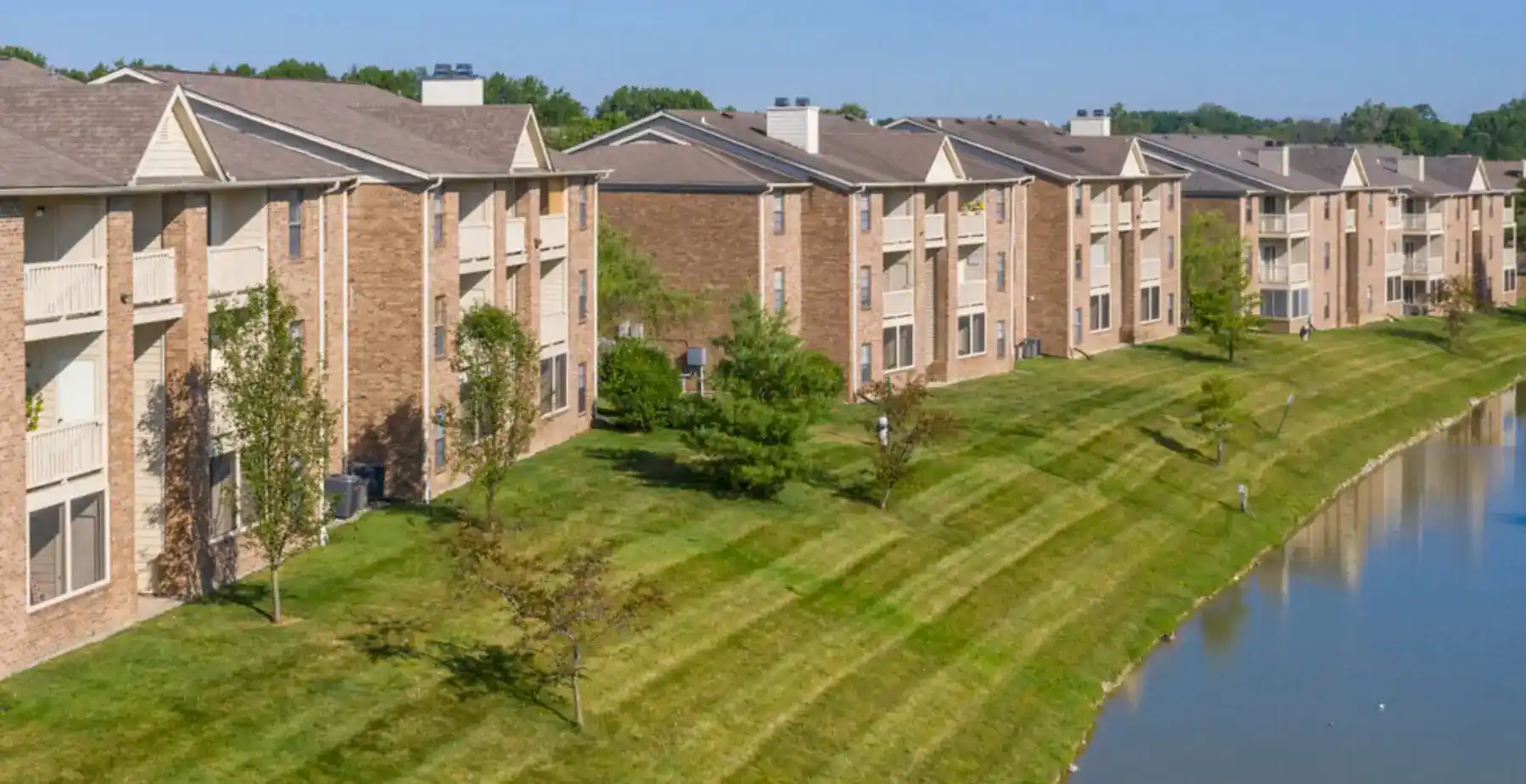 Drone exterior view of the Woodspring Apartments buildings on lush, manicured lakeside grounds